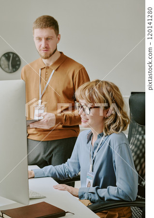 Vertical shot of young Caucasian man and woman discussing plan while looking at computer screen at work in modern office Vertical shot of young Caucasian man and woman discussing plan while looking at computer screen at work in modern office 120141280