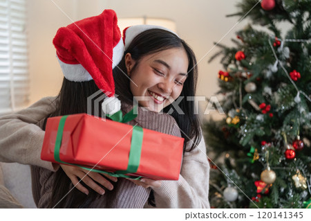 Joyful Young Woman Couple Exchanging Surprise Gift Box by Christmas Tree in Festive Holiday Celebration 120141345
