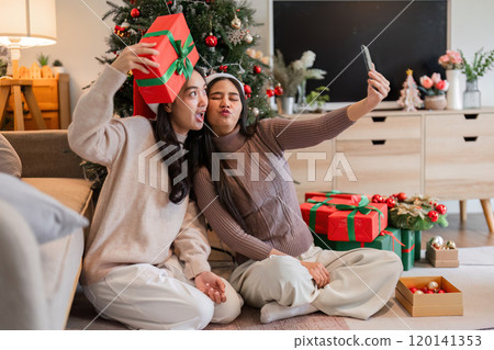 Young Woman Couple Celebrates Christmas with Surprise Gift Box in Festive Holiday Setting by the Christmas Tree 120141353