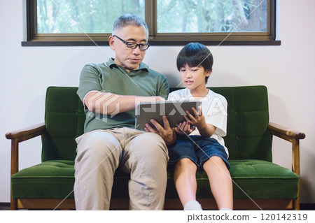 Grandson and grandfather enjoying a tablet together at home Grandson and grandfather enjoying a tablet together at home 120142319