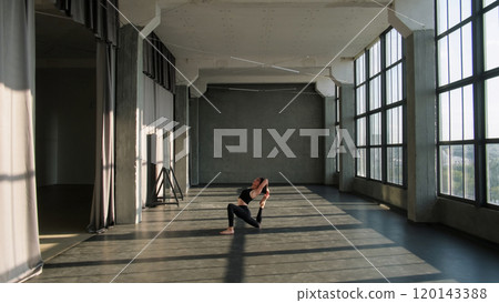 Gymnastic pose. Stretch practice. Fit woman in activewear training yoga flexibility exercise physical workout alone in empty gym fitness studio loft interior. 120143388
