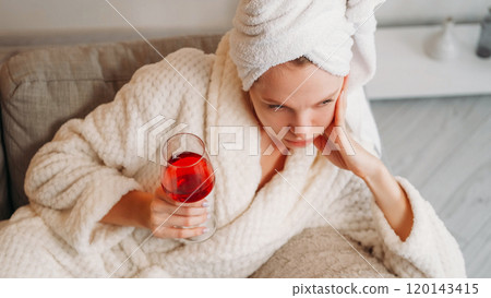 Woman thoughtfulness. Mind rest. Tired pensive young lady in white bath spa towel and soft robe holding glass with red tasty wine after shower. 120143415