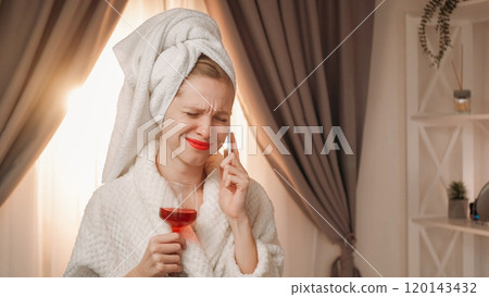 Wine tasting. Online discussion. Attractive young woman with makeup in white bath towel and bathrobe holding glass with red drink after shower while talking phone. 120143432