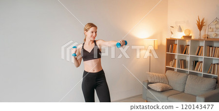 Weight lifting. Muscle stretching. Contented smiling trim girl using dumbbells at home showcasing power and dedication to fitness. Weight lifting. Muscle stretching. Contented smiling trim girl using dumbbells at home showcasing power and dedication to fitness. 120143477