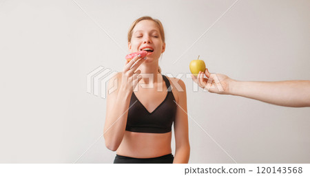 Dieting story. Unhealthy food. Slim young confused woman in black modern suit choosing between apple and cream cake on white background. Dieting story. Unhealthy food. Slim young confused woman in black modern suit choosing between apple and cream cake on white background. 120143568