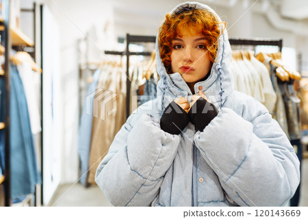 young attractive red-haired woman trying on a warm jacket 120143669