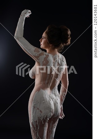 Artistic model posing with body paint in a dramatic, dark studio setting Artistic model posing with body paint in a dramatic, dark studio setting 120143681