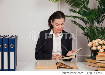 Woman in business attire working at desk with books in university office Woman in business attire working at desk with books in university office 120144258