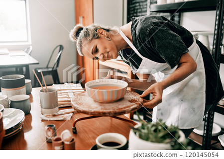 I spend time perfecting my art. Cropped shot of an attractive mature woman standing alone and painting a pottery bowl in her workshop. 120145054