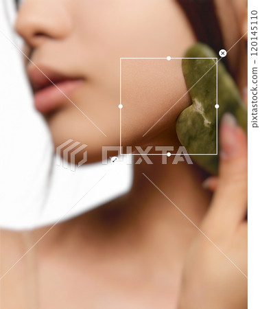 Close-up cropped image of female face, using gua sha massage tool. Woman doing facial massage. Face building. 120145110