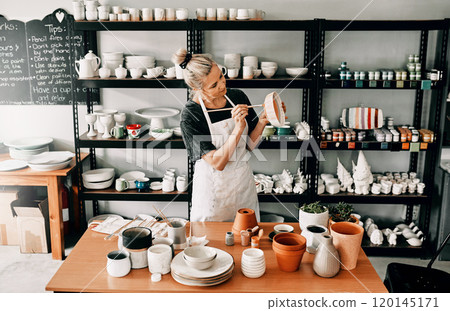 Adding a final and personal touch. Cropped shot of an attractive mature woman standing alone and painting a pottery bowl in her workshop. 120145171
