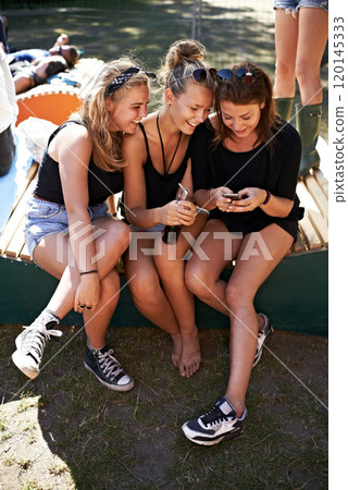 I cant believe that cute guy texted me. Three friends sitting together and sharing gossip at a music festival. 120145333