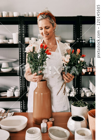 These flowers look perfect in my vase. Cropped shot of an attractive mature woman standing alone and putting flowers into a handmade vase in her pottery workshop. 120145685
