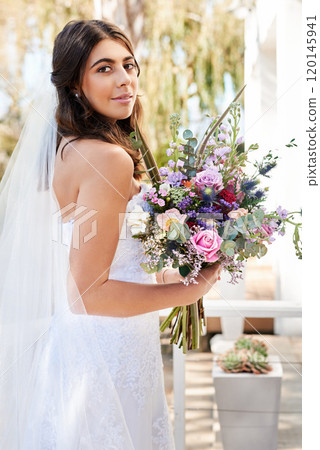 She looks absolutely mesmerizing on her wedding day. Portrait of a happy and beautiful young bride holding a bouquet of flowers while posing outdoors on her wedding day. 120145941