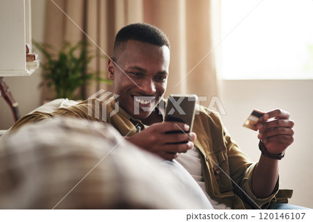 Did I just get a free delivery. Cropped shot of a handsome young man smiling while using a smartphone and a credit card to shop online in his living room at home. Did I just get a free delivery. Cropped shot of a handsome young man smiling while using a smartphone and a credit card to shop online in his living room at home. 120146107