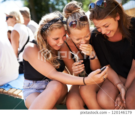 Girls getting in on the gossip. A group of three young girls huddled together and laughing while looking at a cell phone. 120146179