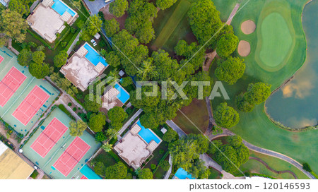 Scenic top-down view of a resort complex featuring villas, swimming pools, and tennis courts amid a tranquil natural setting. 120146593
