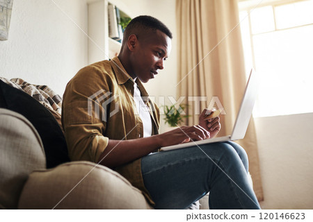 Because its a perfect day to splurge a little. Cropped shot of a handsome young man using a laptop and a credit card to shop online while sitting on his couch at home. 120146623