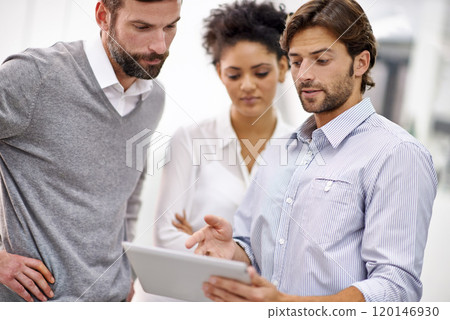 Going over the projects online presence. Shot of three young businesspeople standing in his office and talking over a tablet. 120146930