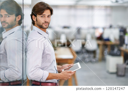 Hes a confident young businessman. Portrait of a handsome young businessman standing in his office holding a tablet. 120147247