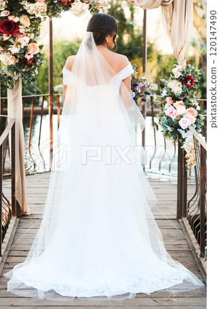 The wait is finally over. Rearview shot a beautiful young bride standing outdoors on her wedding day. 120147490