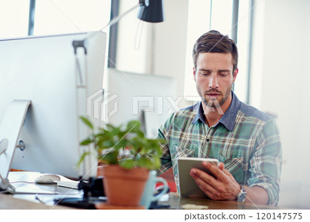 My mobile office. Shot of a casually-dressed young man using a digital tablet at his desk. 120147575
