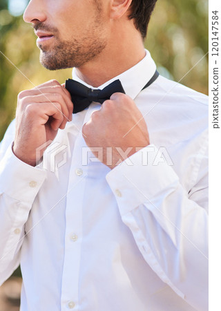Now Im ready. Cropped shot of an unrecognizable young bridegroom putting on a bowtie while standing outdoors on his wedding day. 120147584