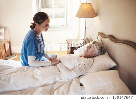 The friendliest face to wake up to. Shot of a young nurse chatting with a senior woman in bed at a retirement home. 120147647