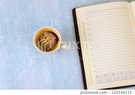 Coffee espresso steams on light blue surface next to an open notebook planner. Coffee espresso steams on light blue surface next to an open notebook planner. 120148215