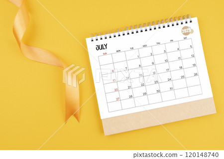 July 2025 desk calendar with yellow ribbon on yellow background. 120148740