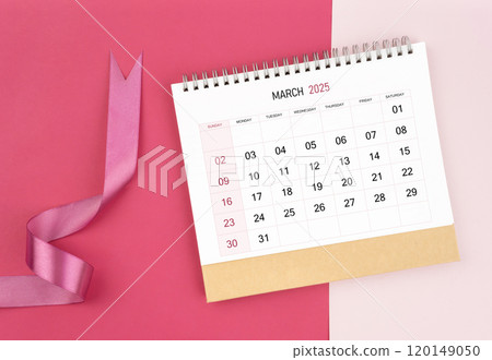 March 2025 desk calendar and pink ribbon on pink background. 120149050