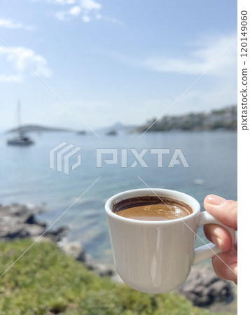 hand holds cup of coffee over sea and island under blue sky 120149060