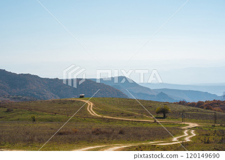 Serene winding dirt road through green hills under a clear blue sky in a tranquil countryside setting Serene winding dirt road through green hills under a clear blue sky in a tranquil countryside setting 120149690