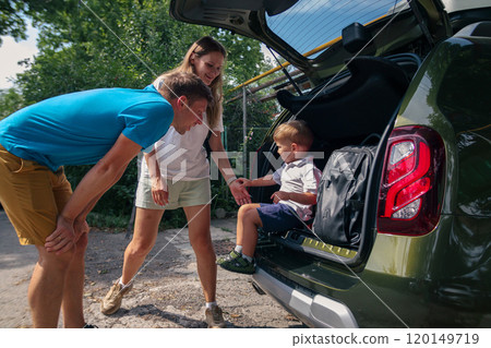 A cheerful family happily packs their car for an exciting outdoor adventure, engaging joyfully with their young child 120149719