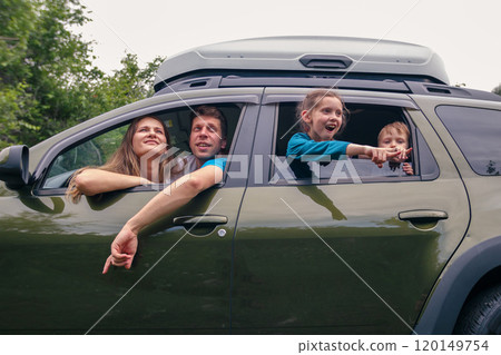 A cheerful family is enjoying a funfilled road trip, sharing laughter and excitement as they travel in a green SUV 120149754