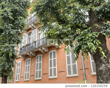 old brick house with closed white window blinds behind trees 120150259