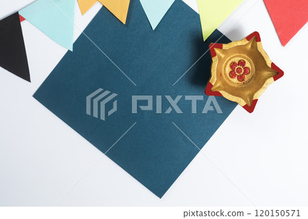 Top View of Golden Diwali Diya, Blank Paper Note, and Colorful Decorative Flags on a White Background. Perfect for Diwali Celebration Themes 120150571