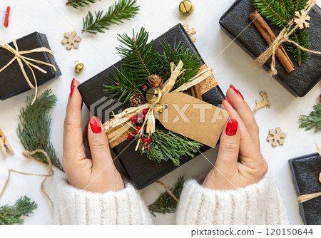 Hands with Christmas present with blank gift tag, box decorated with fir branches, Mockup 120150644