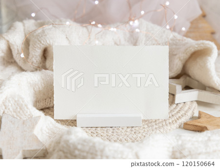 Horizontal paper card near white sweater and wooden Christmas decor and lights, mockup Horizontal paper card near white sweater and wooden Christmas decor and lights, mockup 120150664