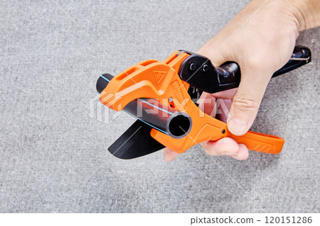 Cutter scissors for plastic pipes are equipped with ratchet mechanism, hand holds plumber tool on background of flat slate. Cutter scissors for plastic pipes are equipped with ratchet mechanism, hand holds plumber tool on background of flat slate. 120151286