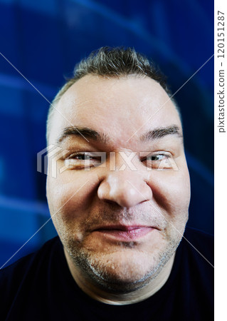 Photographing face with wide-angle lens from close range, 47 year old Caucasian man with an excess weight problem, portrait on blue background. Photographing face with wide-angle lens from close range, 47 year old Caucasian man with an excess weight problem, portrait on blue background. 120151287
