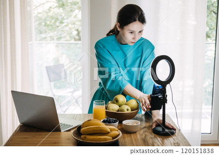Young woman filming healthy lifestyle content with fruits and juice in kitchen. Wellness blogging and influencer marketing concept Young woman filming healthy lifestyle content with fruits and juice in kitchen. Wellness blogging and influencer marketing concept 120151838