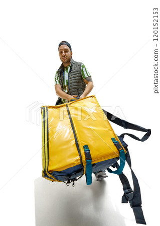 Wide angle photo of young man, courier, dressed casually and carrying huge food delivery pack against white studio background. 120152153