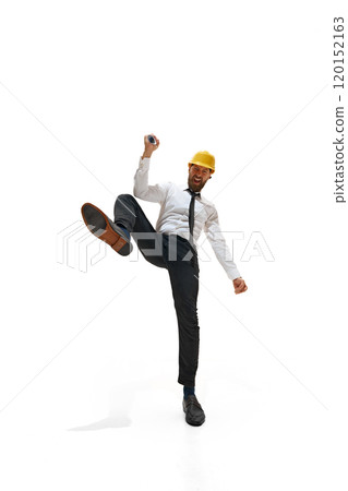 Young man dressed formal wear with builder-helmet shouting of joy and clenching fists against white studio background. 120152163