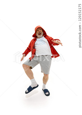 Pensioner, dressed red jacket, shorts and slippers dancing raising legs against white studio background. Excited mature man. 120152175