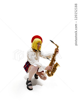 Woman with yellow wig crouching, holding saxophone, wearing red beret, white blouse, and plaid skirt against white studio background. 120152188
