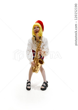 Woman with yellow wig and red beret, wearing plaid skirt, posing with saxophone, looking upward wit playful expression against white studio background. 120152190