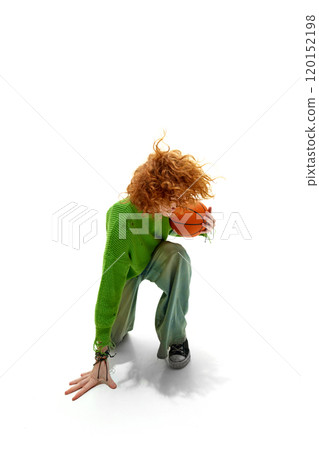 Red-haired man in green hoodie and jeans strike low pose with basketball against white studio background. 120152198