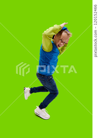 Little boy, dressed casual attire running energetically with smile on his face against vibrant green background. Little boy, dressed casual attire running energetically with smile on his face against vibrant green background. 120152466