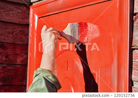 Flat paint brush 100 mm wide is used to paint front door of wooden farmhouse red. 120152736
